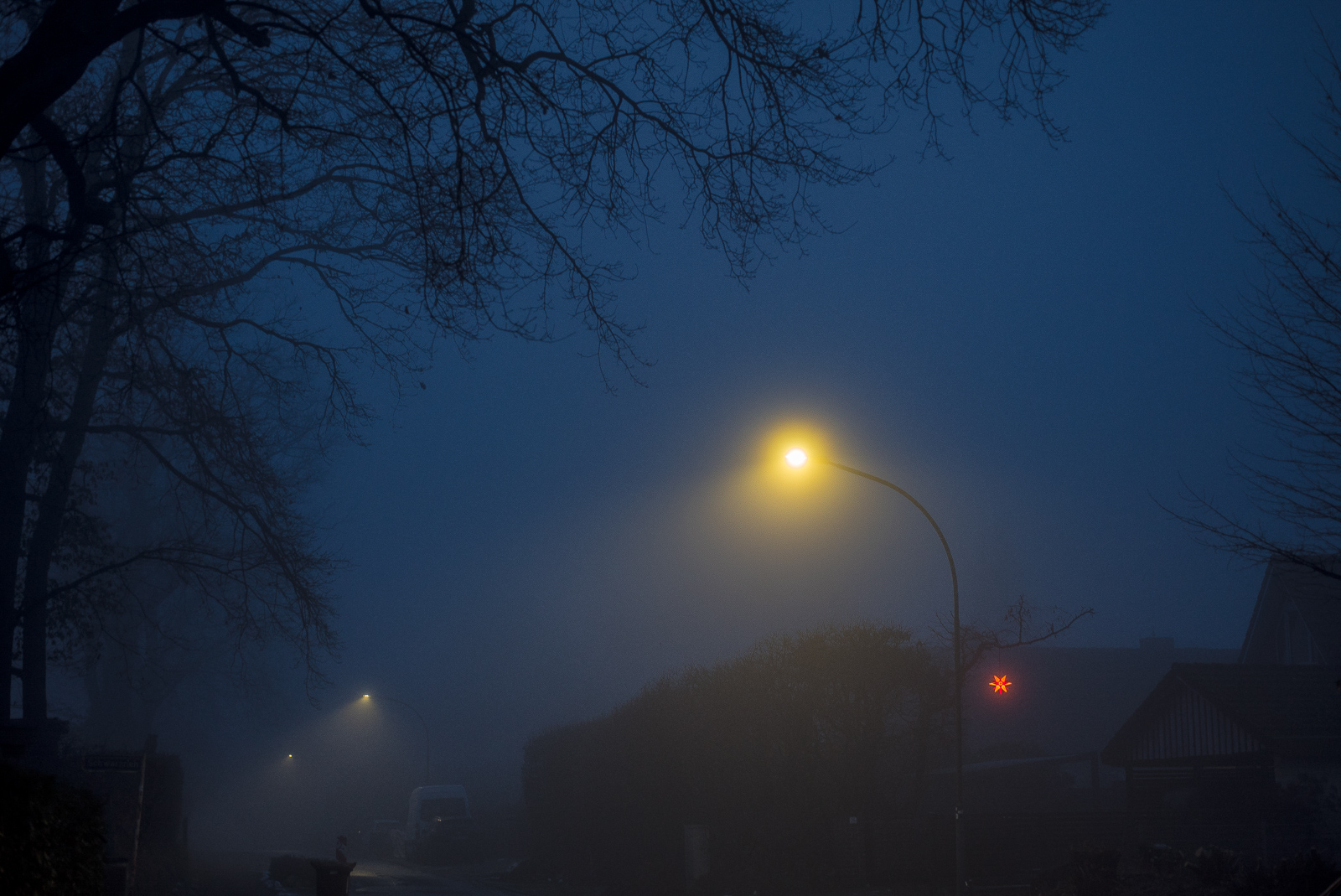 Abendlicher Nebel in blauem Dämmerlicht: Straßenlaternen und ein rot leuchtender Stern