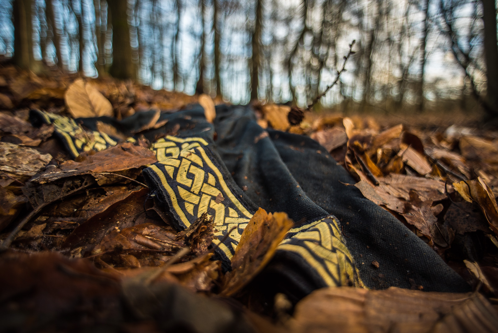 Ein Stück schwarzen Stoffs mit keltischem Flechtmuster in Gold liegt auf dem Waldboden