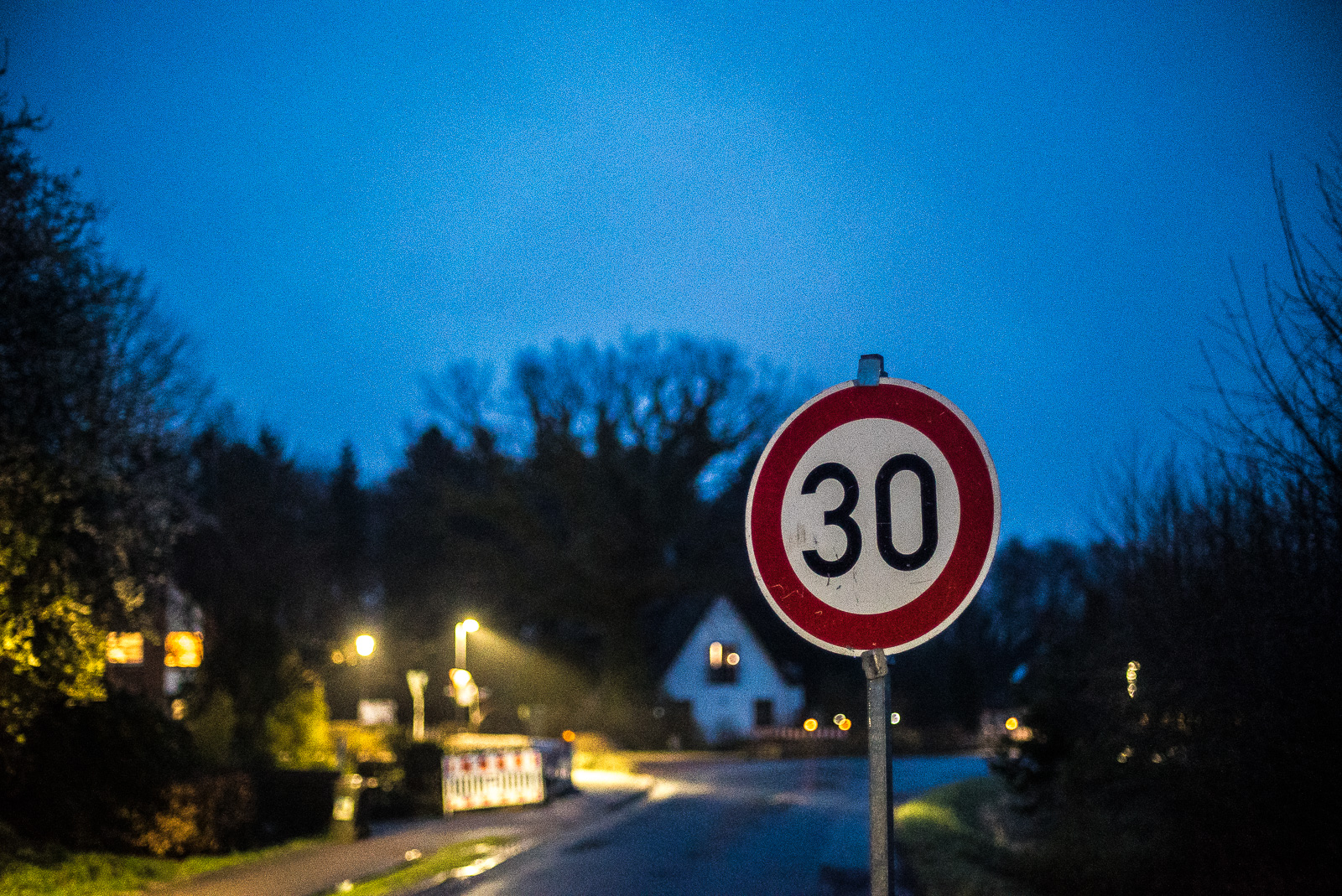 Abendszene einer Dorfstraße mit Baustelle, vorn rechts in der Schärfe ein Verkehrsschild "30"