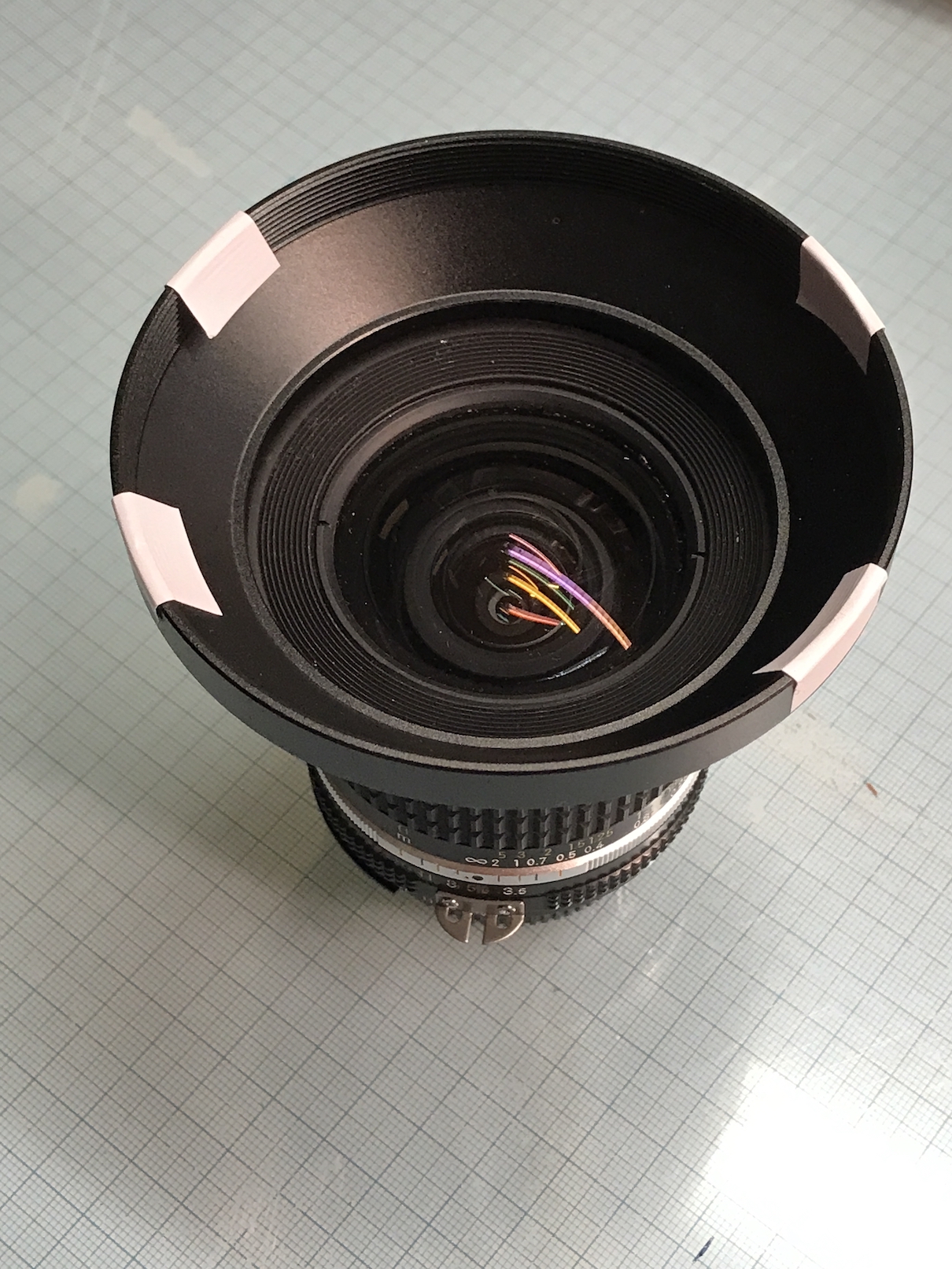 Ein Foto-Objektiv mit einer Streulichtblende, bei der an vier Stellen weiße Sticker angebracht sind.