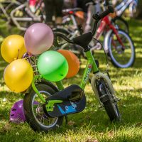 Ein grünes Kleinkinder-Fahrrad auf einer Wiese, dekoriert mit diversen Luftballons
