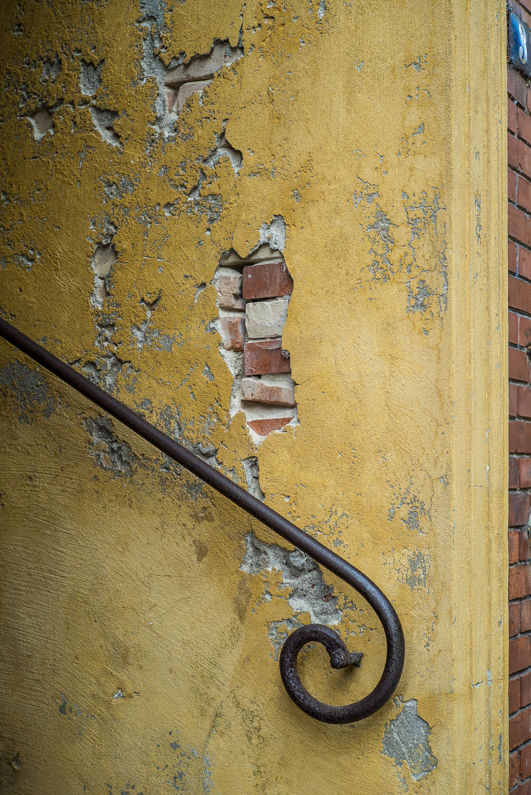 Handlauf einer Treppe vor bröckeligem gelbem Putz auf Mauerstein