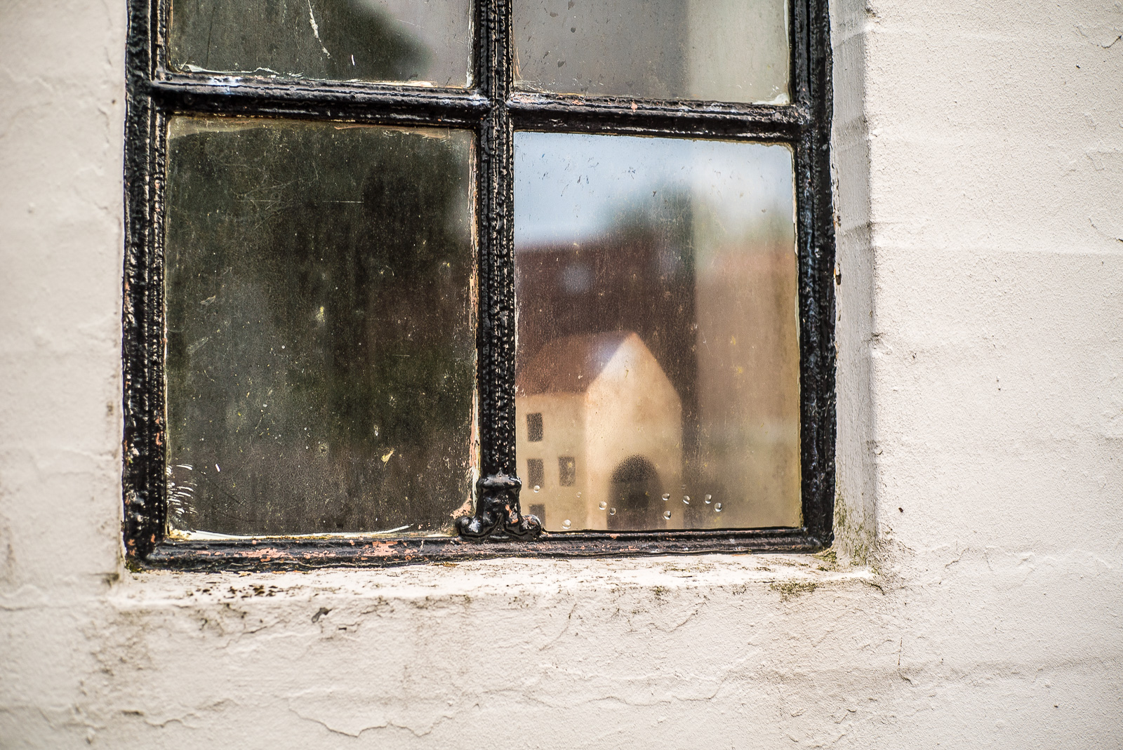 Ein altes metallgefasstes Fenster in weiß geputzter Wand, darin das Modell eines Hauses