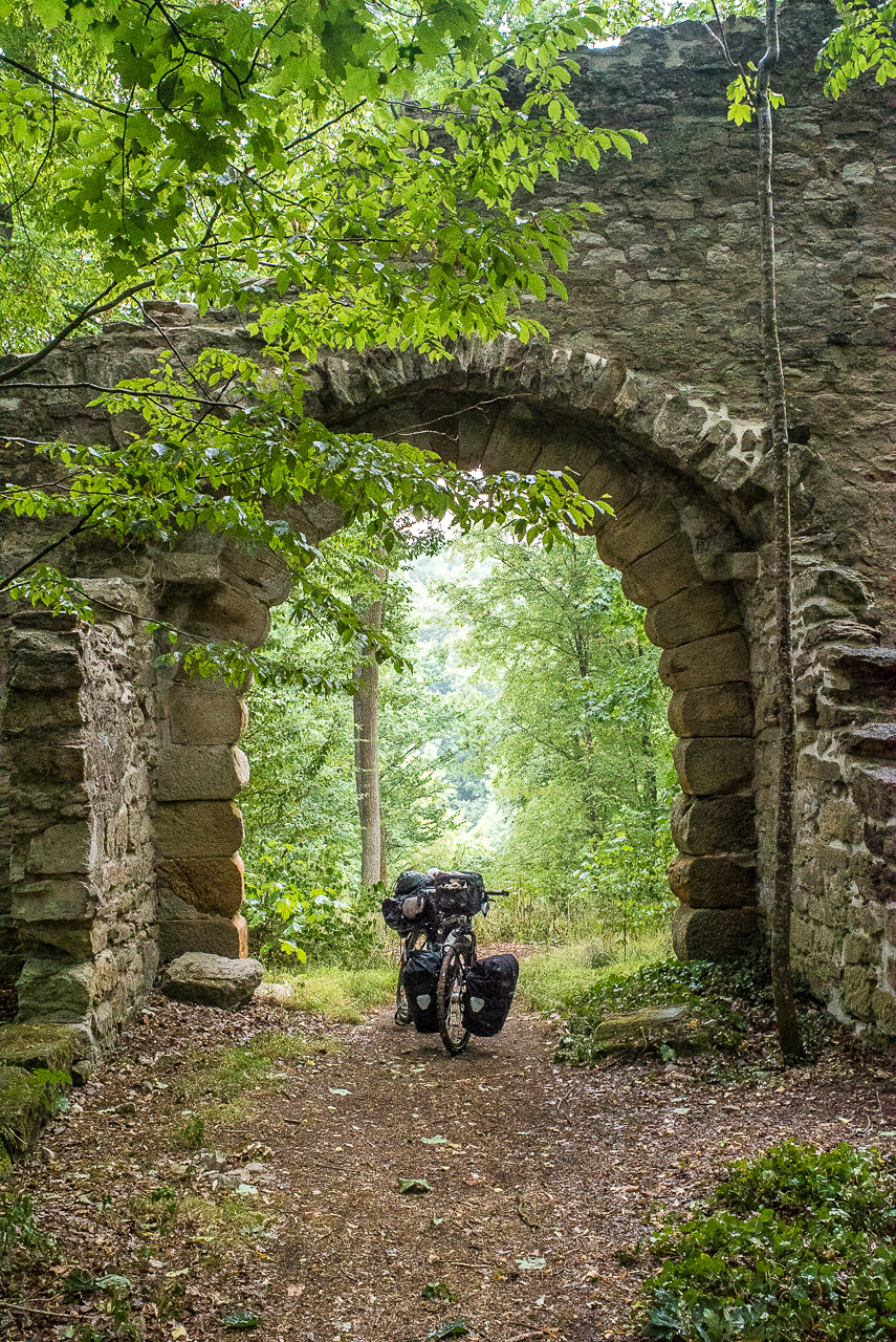 Ein Fahrrad steht unter dem Torbogen einer Ruine im Wald