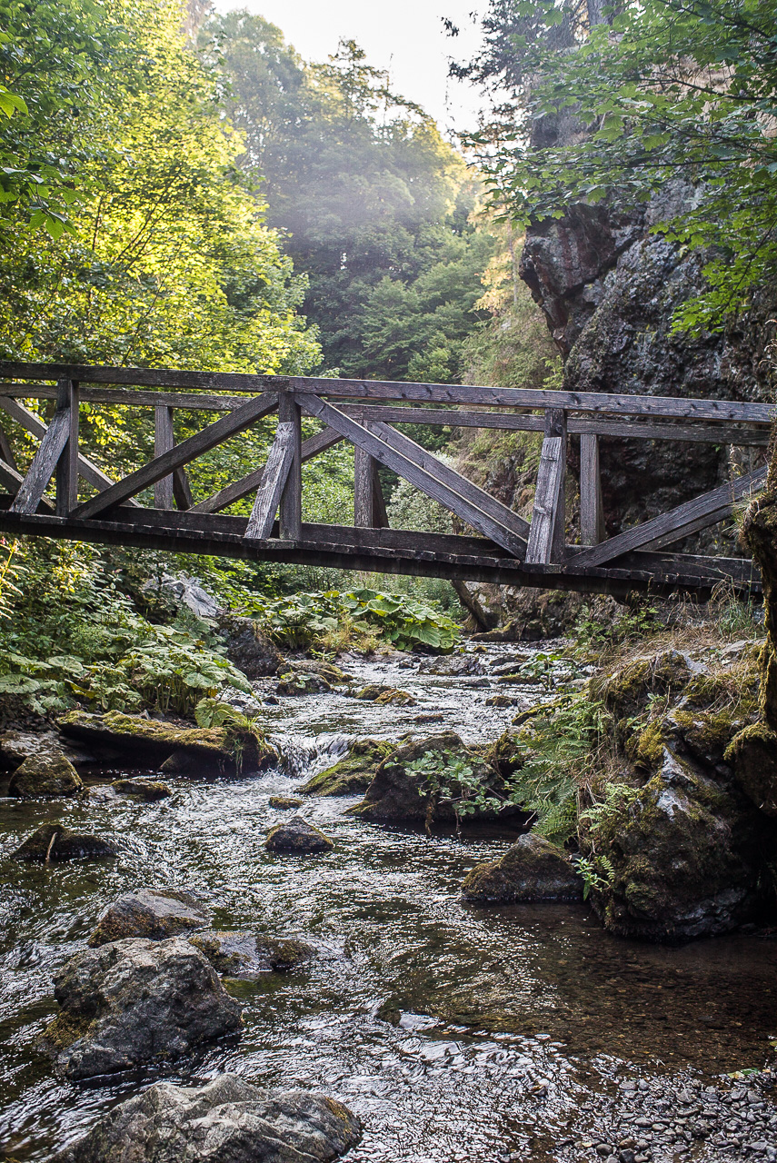 Eine Holzbrücke spannt sich über einen Bach in felsiger Landschaft