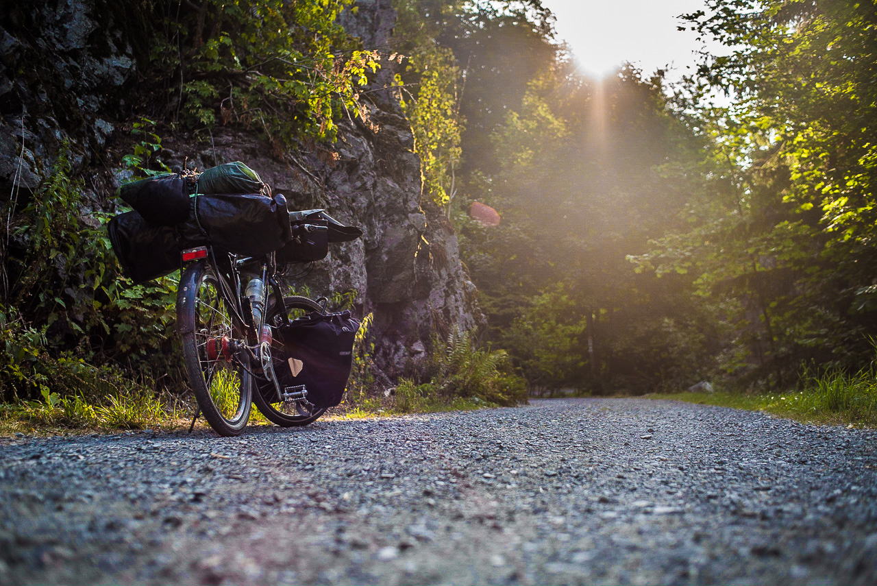 Ein Fahrrad auf einer Schotterpiste im felsigen Wald, gegen die Sonne in Froschperspektive