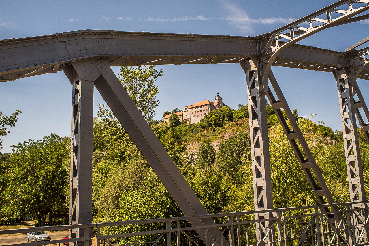 Durch ein Stahlbrücken-Gerüst fotografierte Ansicht eines Schlosses mit rotem Dach auf einem Hügel
