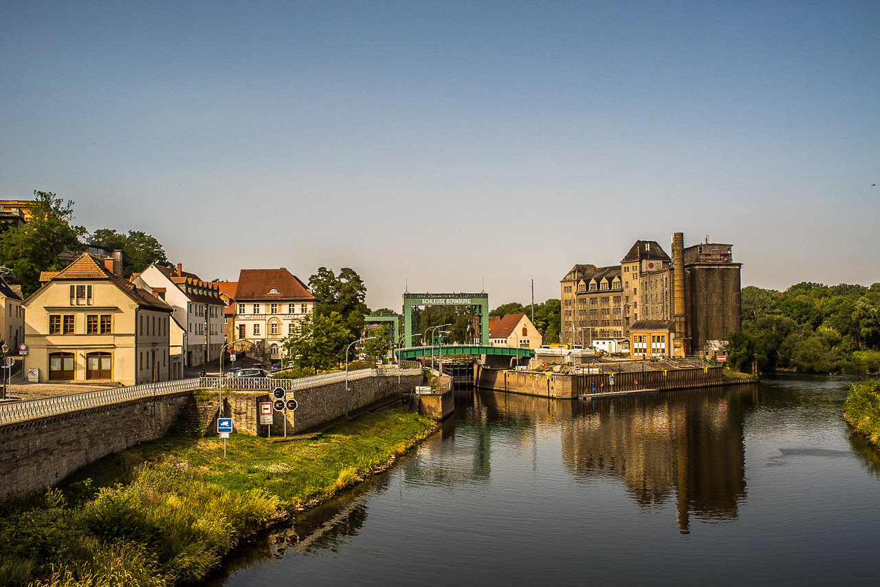 Stadtansicht mit Industriegebäuden am Flussufer, Beschriftung "Schleuse Bernburg"