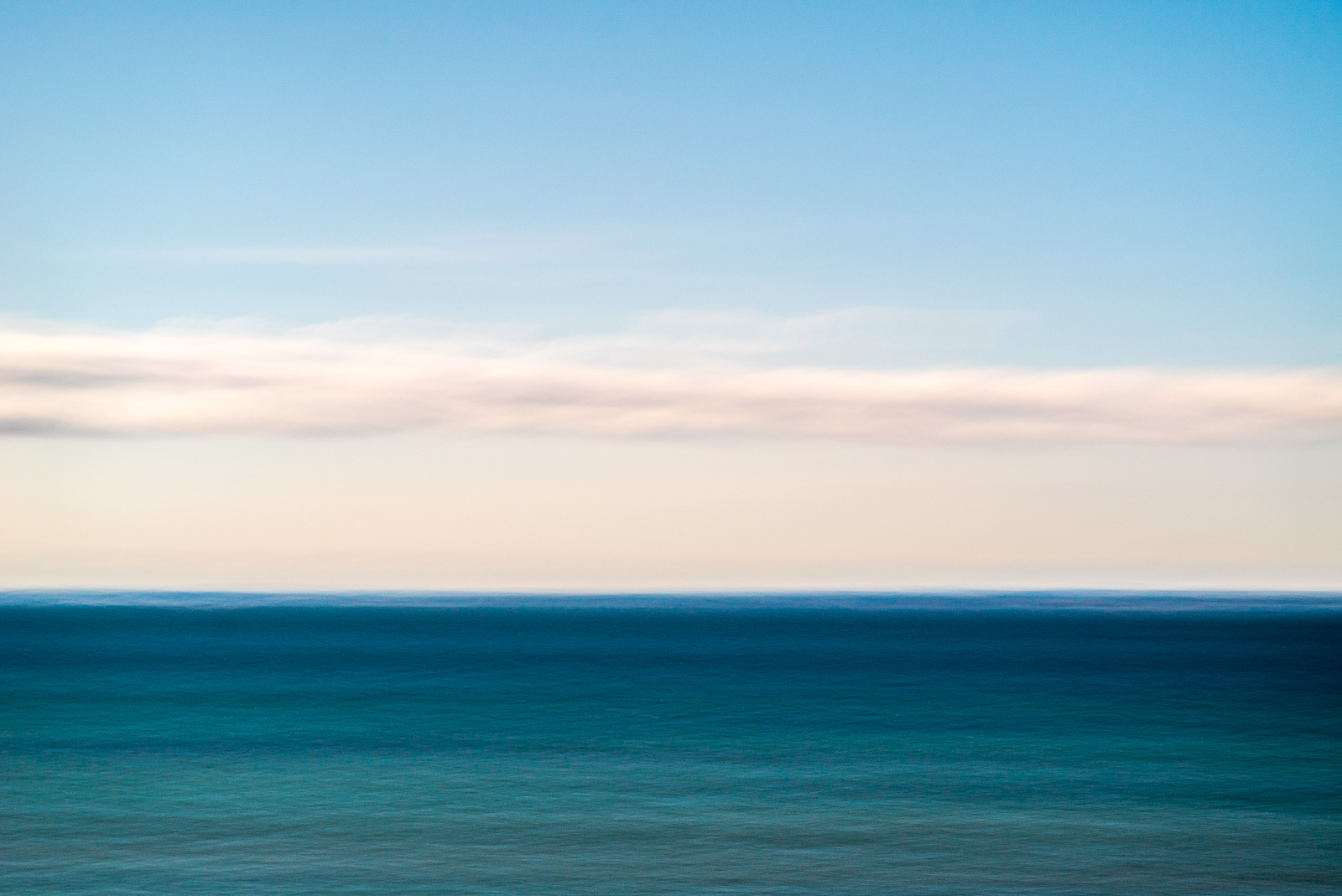 Durch Bewegung verwischtes, abstraktes Bild eines türkisgrünen Meeres mit einem schmalen Wolkenband darüber