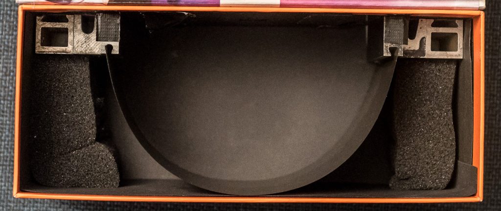 Ein Karton, etwa doppelt so breit wie lang, schwarz ausgekleidet. Mit SchaumStoff und AluProfilen wird ein Stück Foto-AufnahmeMaterial in einem HalbKreis darin eingespannt.