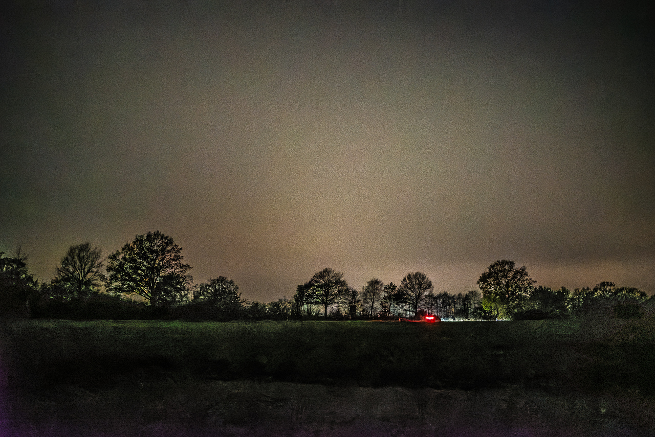 Silhouetten von Bäumen, davor die Rücklichter eines Autos, rötlich leuchtender Himmel