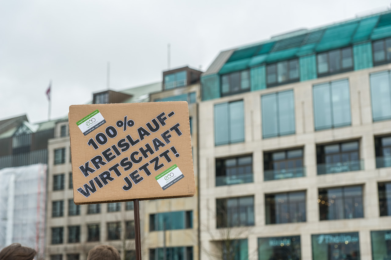 Papp-DemoSchild vor KontorHäusern: 100% Kreislauf-Wirtschaft jetzt!