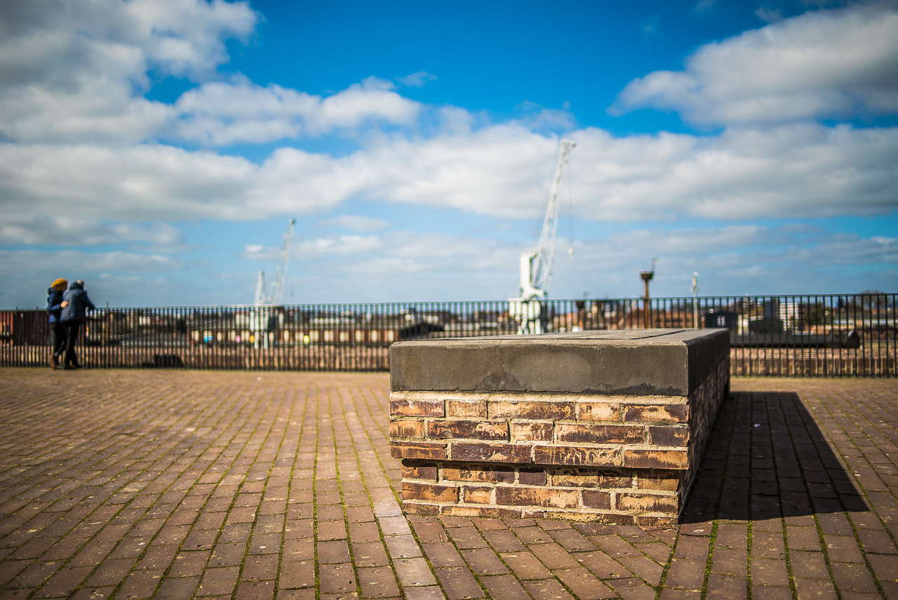 Eine gemauerte AussichtsPlattform über einem Hafen mit Kränen. Links in der Ecke des Bildes ein Pärchen, das hinunter schaut