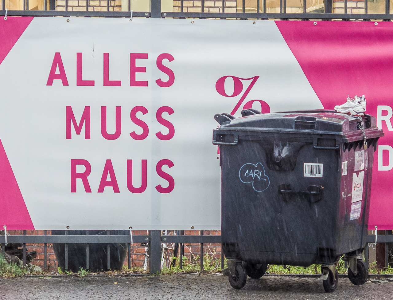 Weiß-pinkes Plakat "Alles muss raus", davor eine Mülltonne