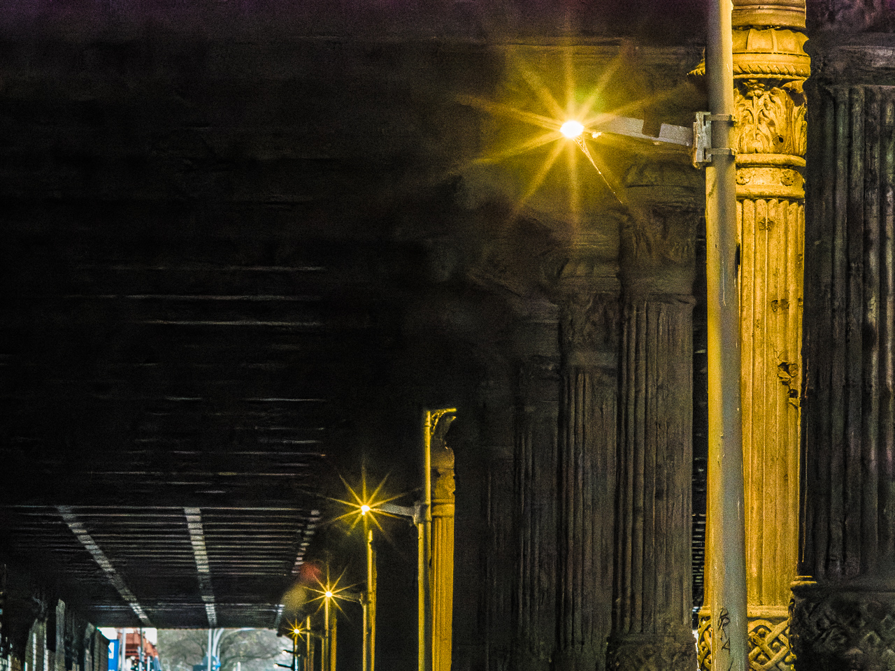 Eine StraßenUnterführung mit alt aussehenden Säulen mit Ornamenten. StraßenLaternen werfen sternförmige Lichter.
