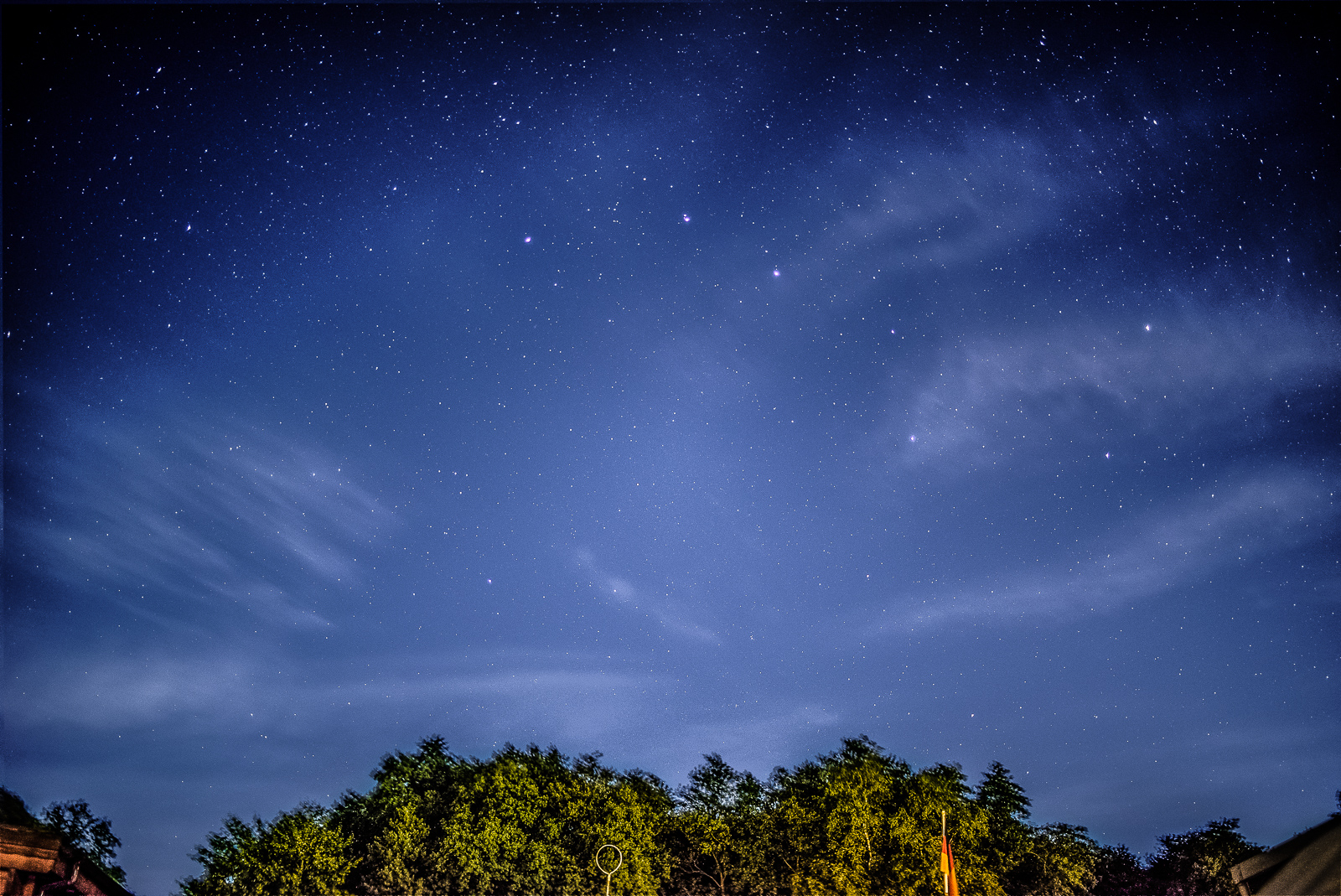 Nachthimmel über einem Stück Wald. Die Sterne sind klar zu sehen, Wolken sind bewegungsUnscharf. Rechts der Mitte deutlich das Sternbild Ursus major, der Große Bär / Großer Wagen.