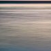 MeeresSpiegel in warmen AbendLicht. Das Foto ist ein enges HochFormat, der unscharfe Horizont liegt etwa an der oberen ViertelTrennung. Darunter weiche, durch sehr lange Belichtung verwischte Wellen, die in der Farbe von dunklem GrünBlau vorn zu pastelligem Gelborange verlaufen. Der Himmel ist ein etwas intensiveres Orange.