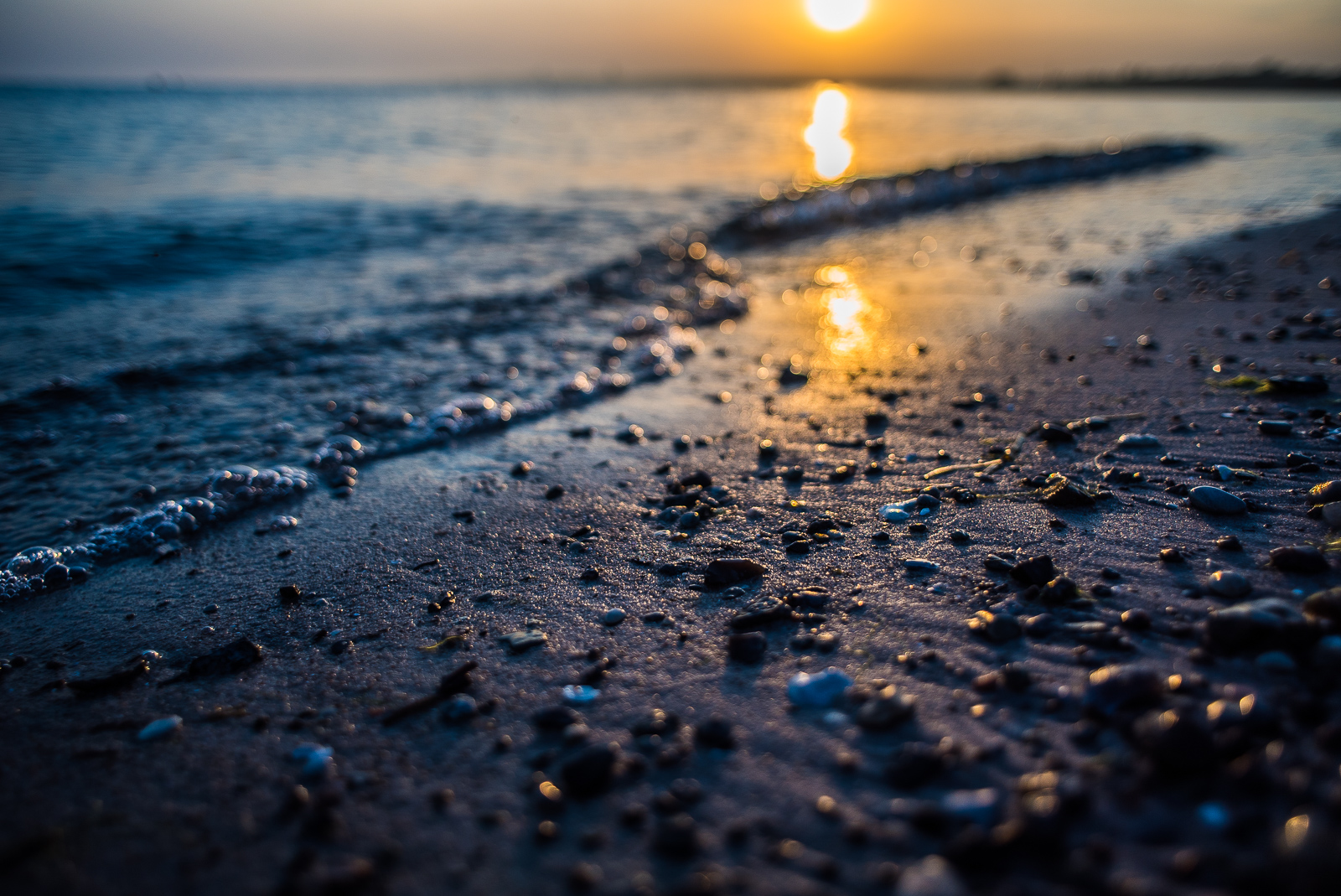 SonnenUntergang am Meer, schräg verlaufender BrandungsSaum und Schärfe auf den kleinen Steinen im VorderGrund