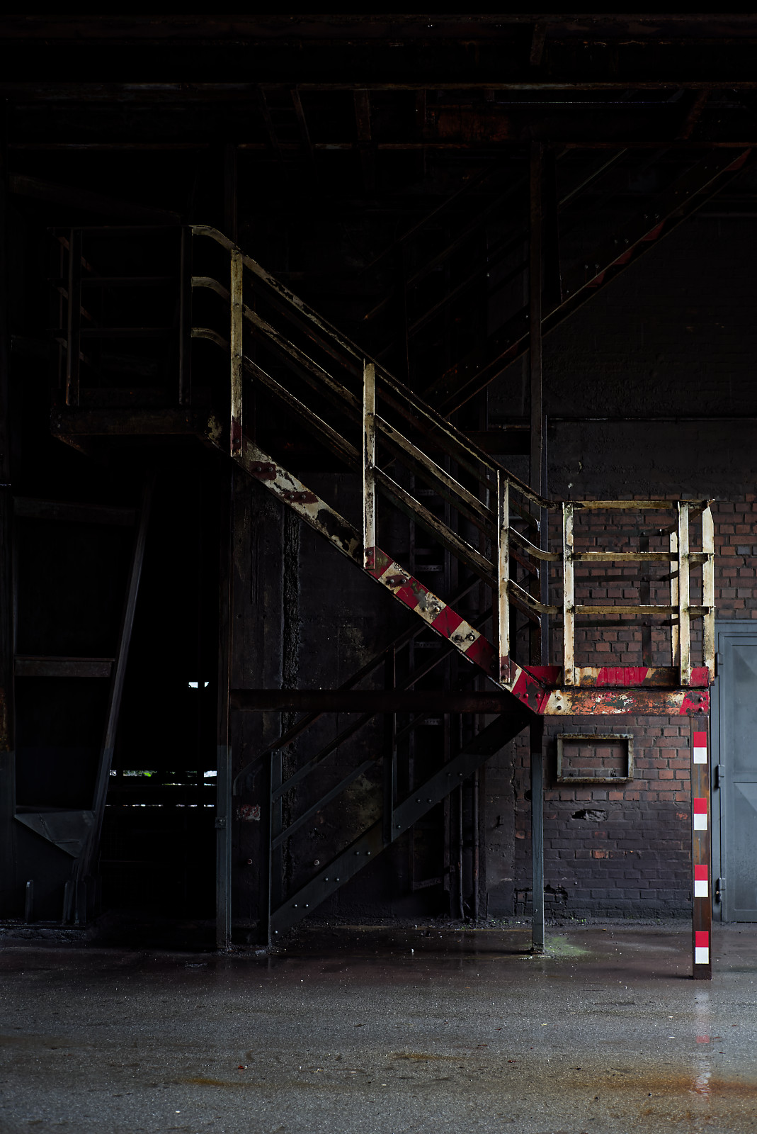 TreppenAufgang in einer IndustrieHalle, weißes Geländer mit roten Streifen, ansonsten sehr dunkel