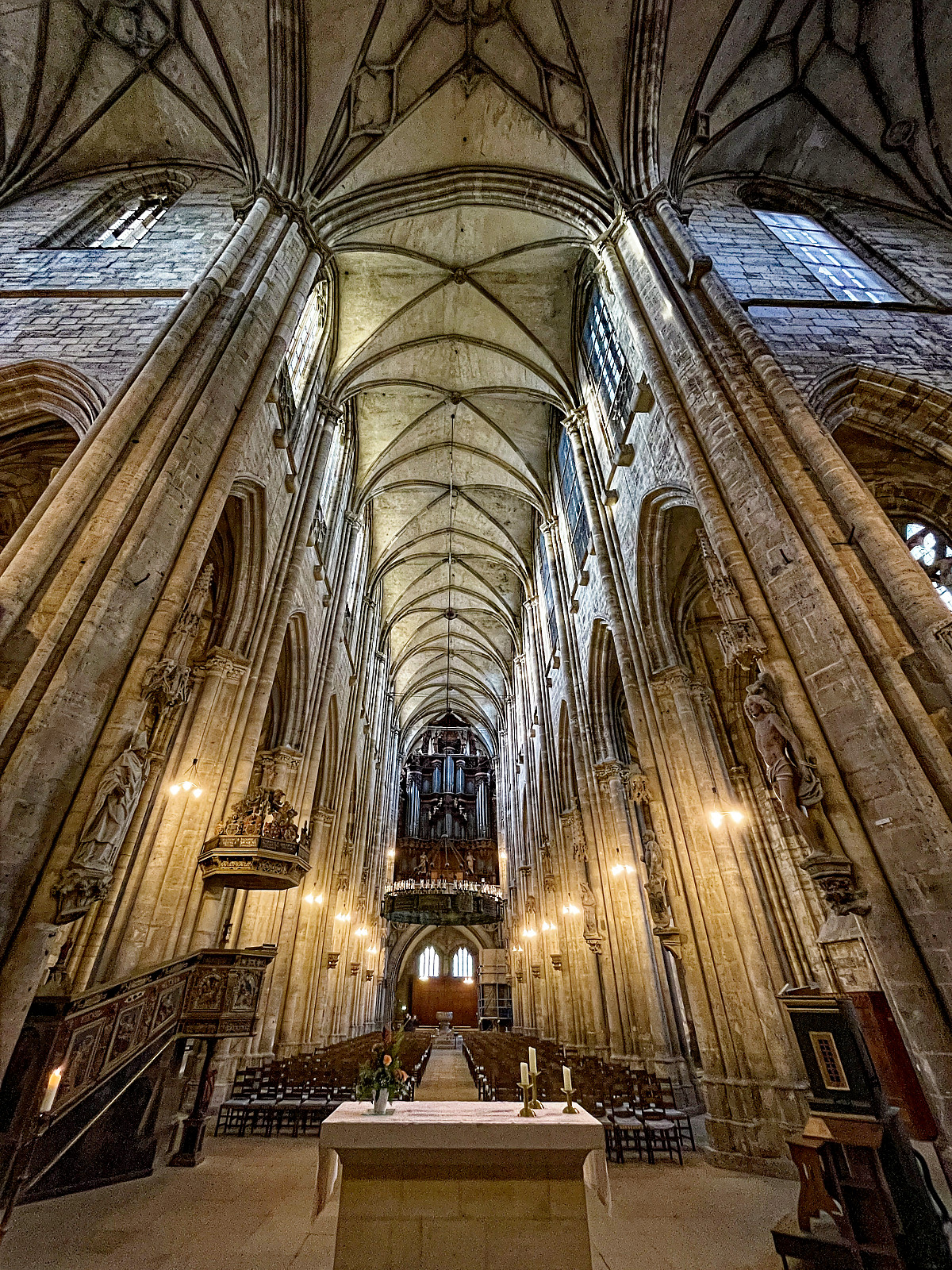InnenAnsicht einer Kathedrale im gotischen Stil mit enorm hohen Säulen aus hellem Stein. Mit Weitwinkel schräg von unten aufgenommen. Im VorderGrund ein schlichter Altar. Am hinteren Ende eine mächtige Orgel.
