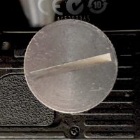 Die UnterSeite einer Kamera im Detail. Zentral ist eine runde Scheibe zu sehen, die erkennbar im StatviGewinde sitzt. Es handelt sich um das KupplungsStück einer Stativ-SchnellWechsel-Einrichtung.